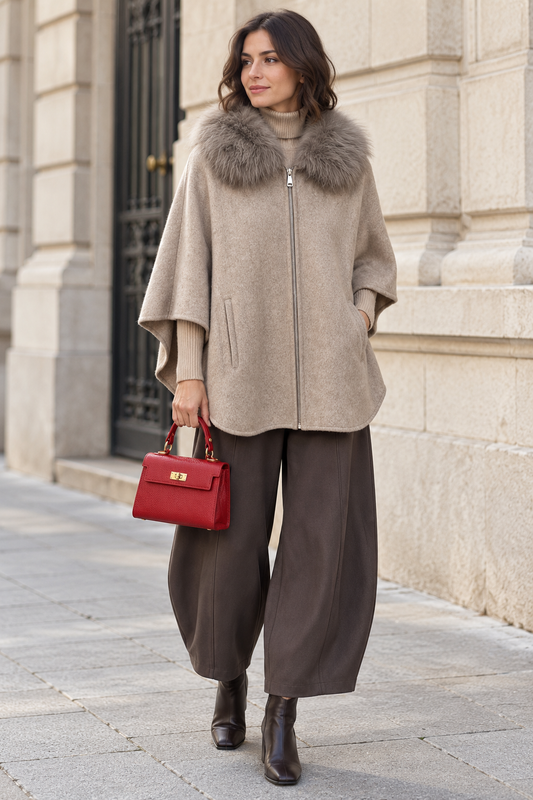 Capa topo con cuello de pelo y cremallera, combinada con jersey beige, pantalón de pernera curva y bolso rojo